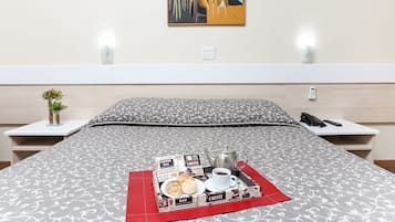 A neatly made bed with a breakfast tray, a coffee pot, and a phone on a bedside table.