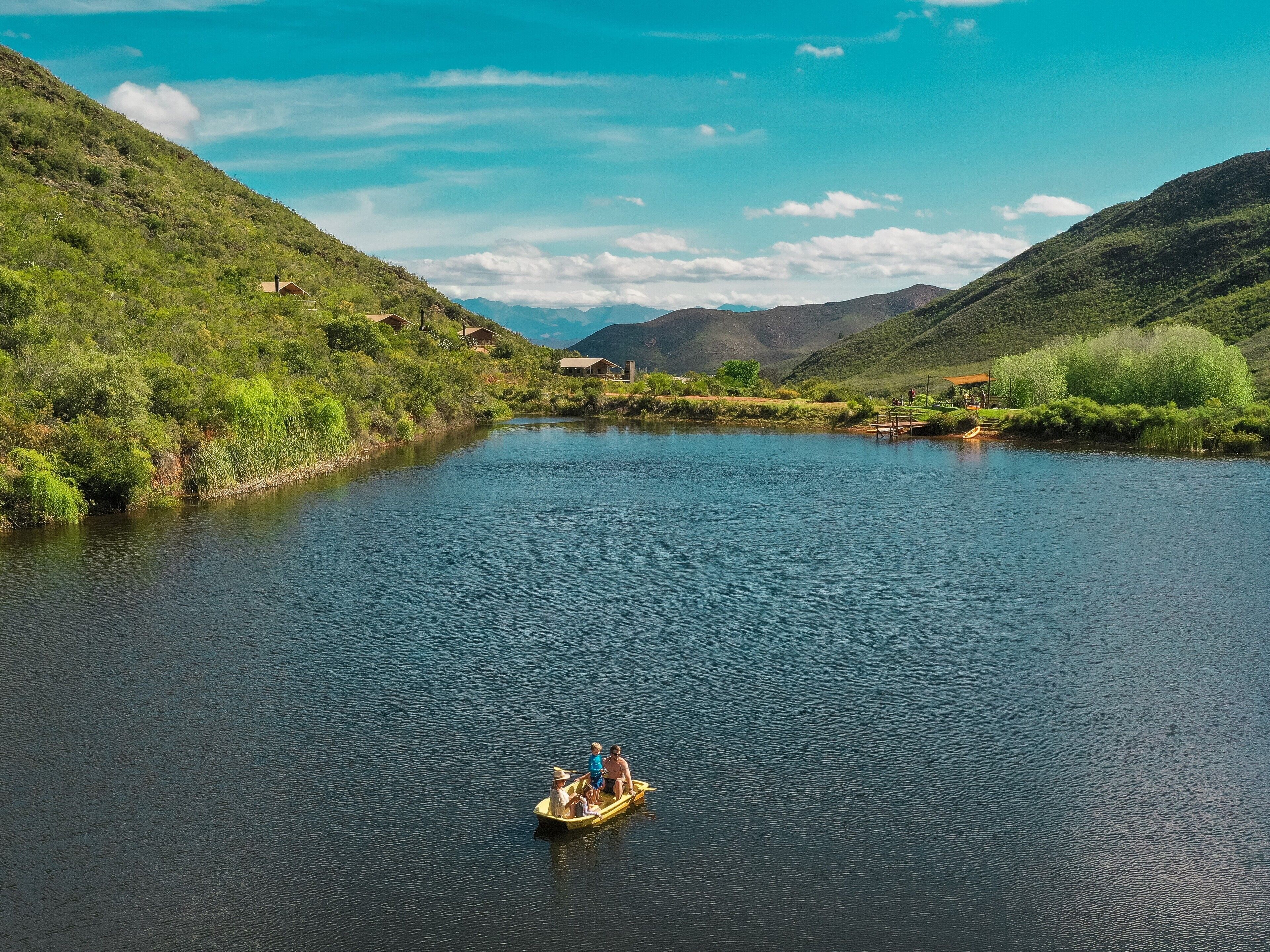 A river with a boat carrying people, surrounded by hills and greenery.
