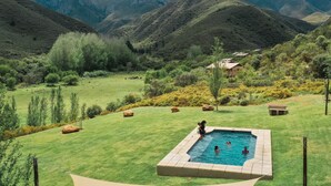 Une piscine entourée d’une pelouse, avec des montagnes en arrière-plan.