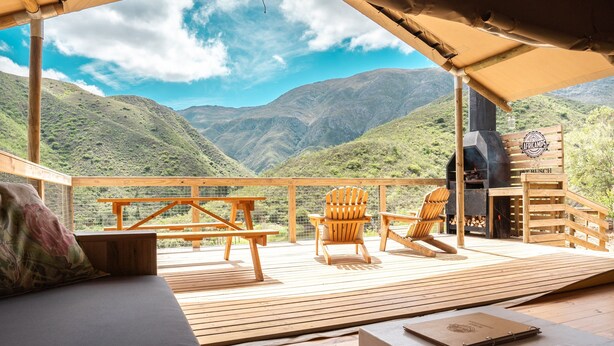 Une terrasse en bois avec un canapé, deux fauteuils Adirondack et un barbecue.
