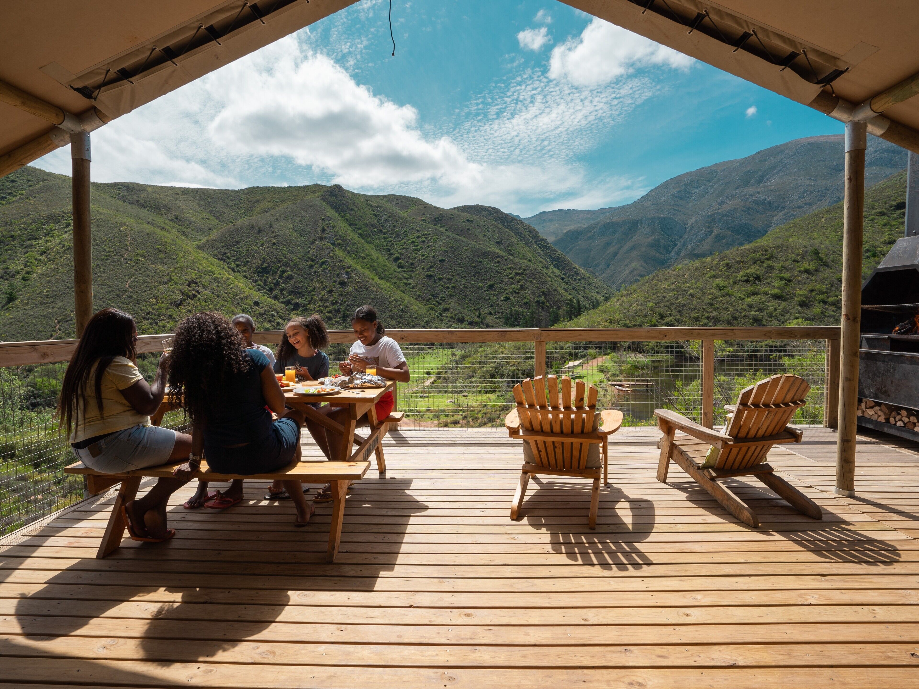 A wooden deck with a table and chairs, overlooking a mountainous landscape.
