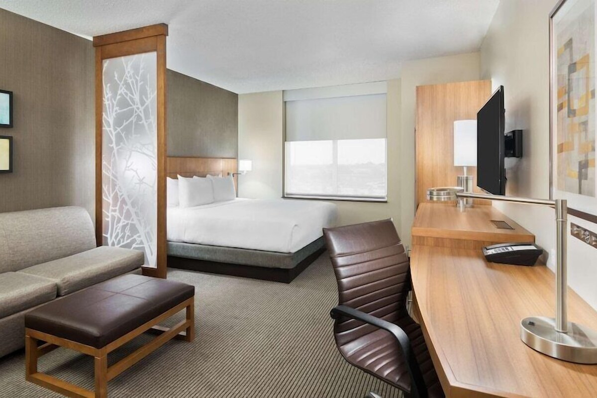 A hotel room with a bed, a sofa, a desk, and a TV.