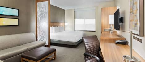 A hotel room with a bed, a sofa, a desk, a chair, a TV, and a window.