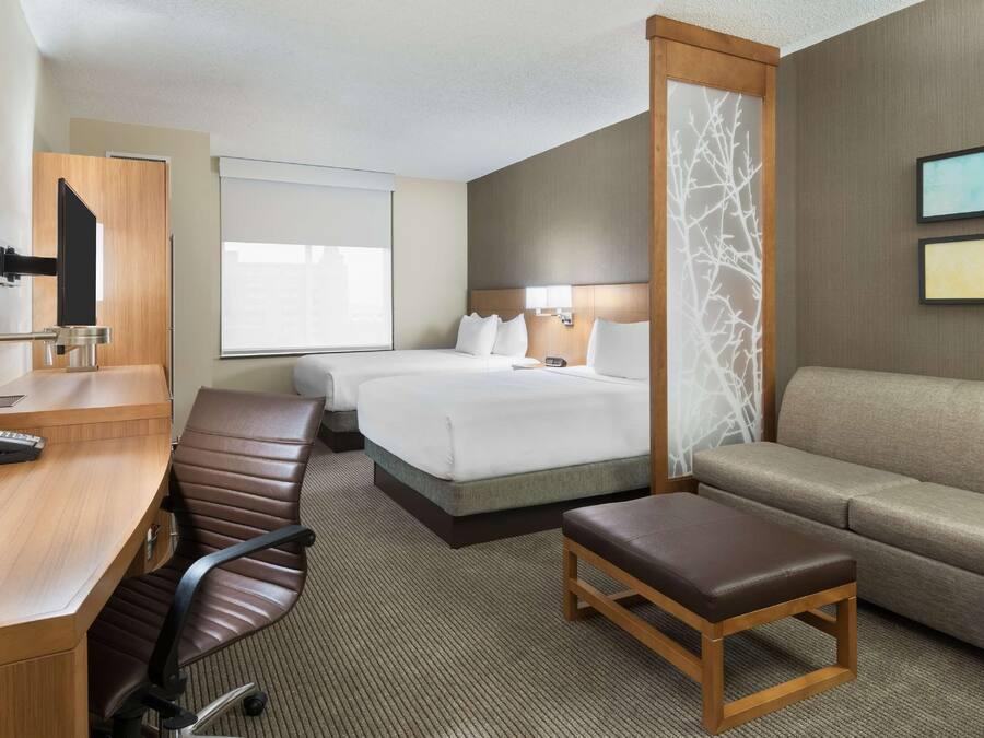 A hotel room with a desk, two beds, a sofa, a chair, and a TV.