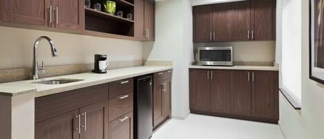 Una cocina moderna con armarios de madera oscura, un lavamanos de acero inoxidable, cafetera, microondas y lavavajillas.