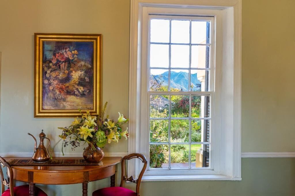 A dining area with a table, chairs, a painting, and a window with a view of greenery and mountains.
