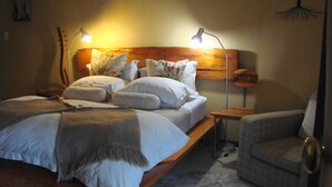 A bedroom with a wooden bed, multiple pillows, a bedside table, a chair, and a lamp. - Die Waenhuis Guest House (George)