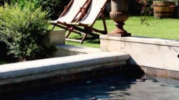 A swimming pool with a stone edge, a lounge chair, and a grassy area in the background. - Die Waenhuis Guest House (George)