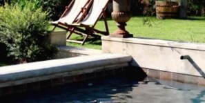 A swimming pool with a stone edge, a lounge chair, and a grassy area in the background. - Die Waenhuis Guest House (George)