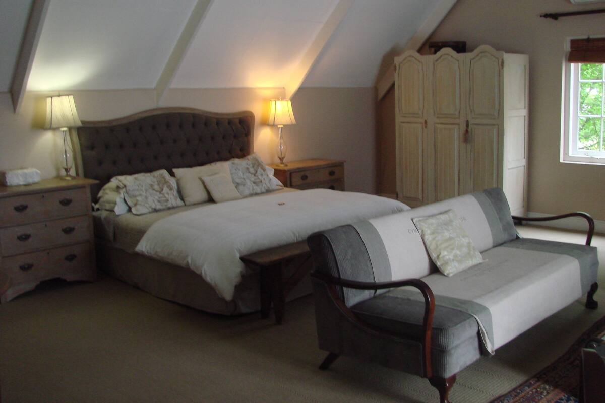 A bedroom with a large bed, a sofa, a wardrobe, and a nightstand with lamps.