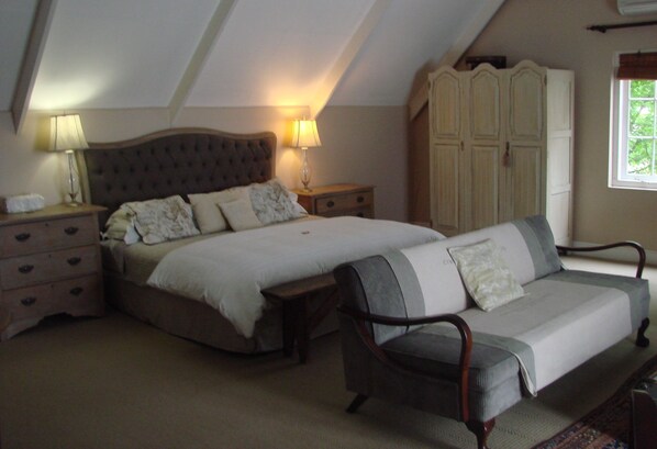 A bedroom with a large bed, a sofa, a wardrobe, and a nightstand with lamps. - Die Waenhuis Guest House (George)