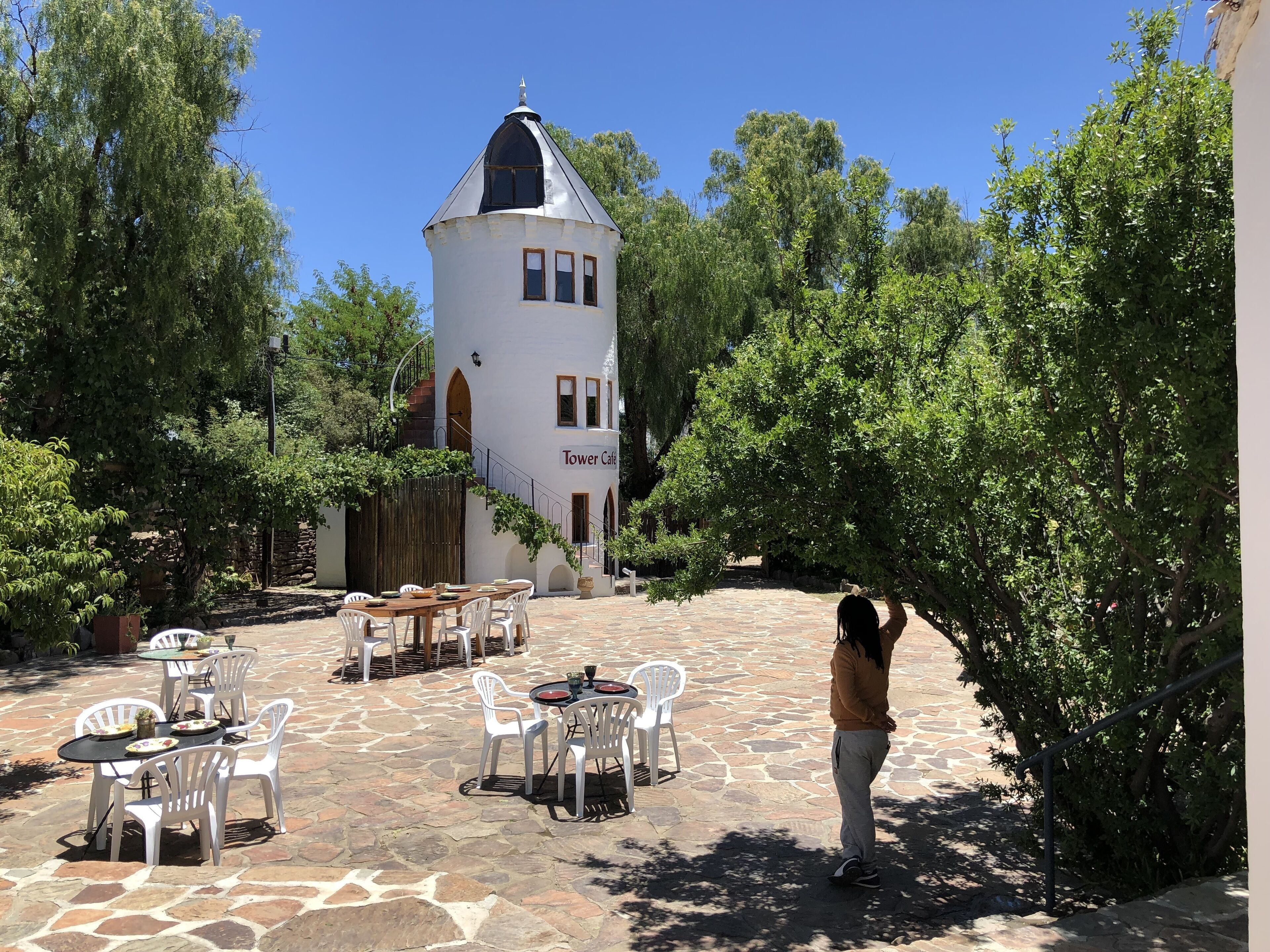 Un patio con suelo de piedra, mobiliario exterior y un edificio blanco con una torre que dice 'Tower Cafe'.