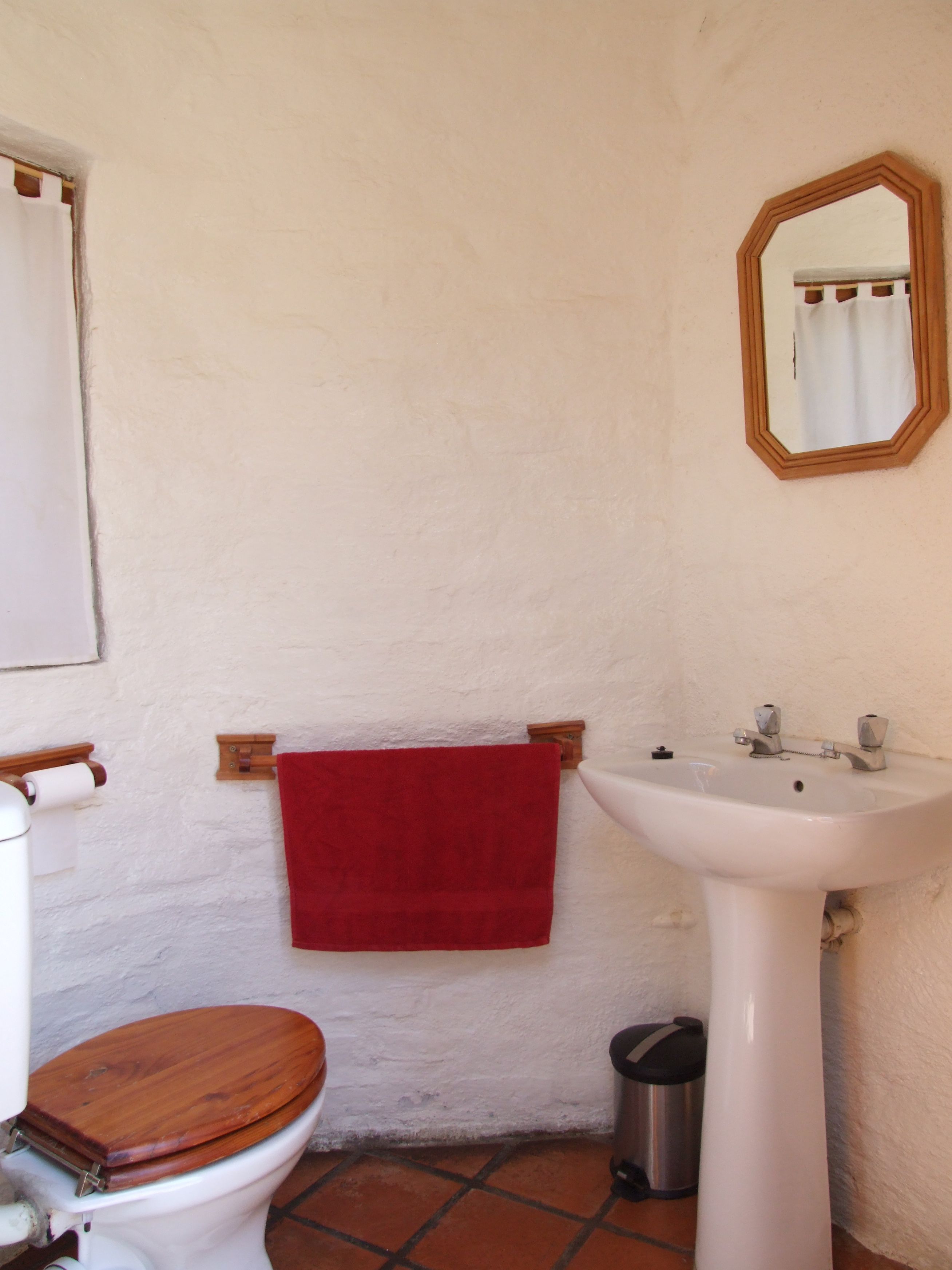 Ein Badezimmer mit einem weißen Waschbecken, einer hölzernen Toilette, einem roten Handtuch und einem Spiegel an der Wand.