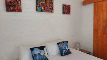 A bedroom with a bed, white pillows, and three colorful paintings on the wall.