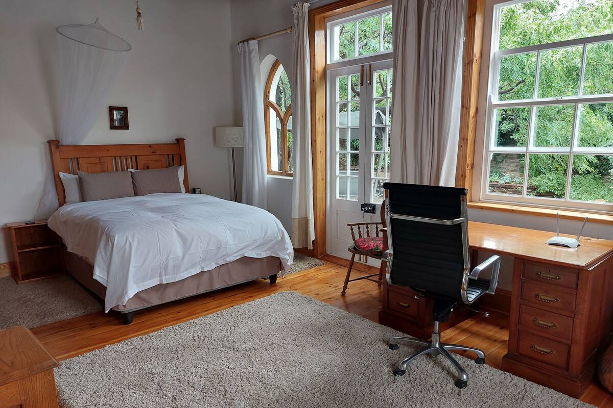 Een slaapkamer met een bed, een bureau, een stoel, een lamp en een raam met gordijnen.