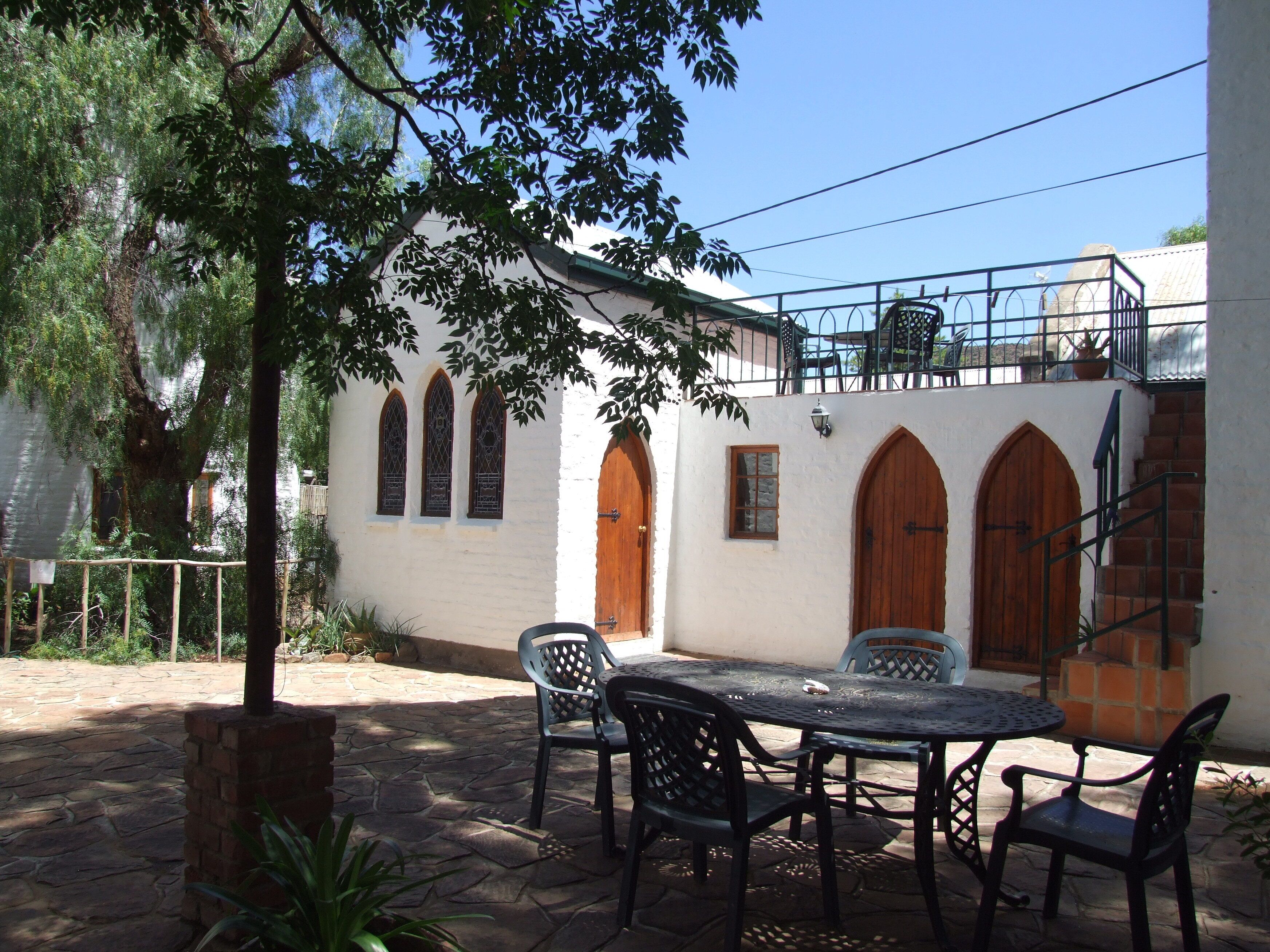 Un patio con piso de piedra, mobiliario exterior y un edificio blanco con ventanas de arco y puertas de madera.