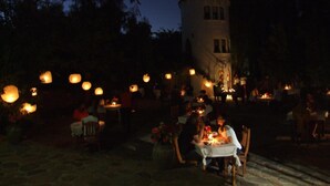 An outdoor dining area with tables and chairs, a tower-like structure in the background, and string lights overhead.