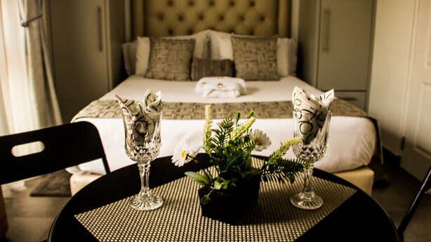 Habitación de hotel con una cama, una mesa de comedor con dos sillas y un florero con flores.