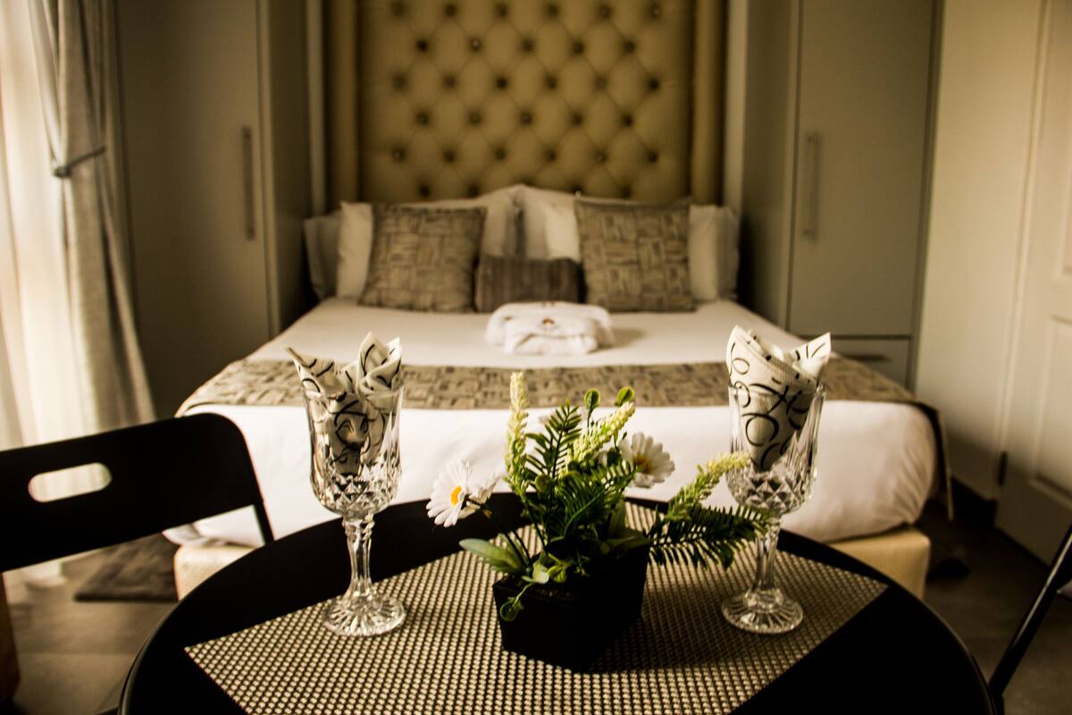A hotel room with a bed, a dining table with two chairs, and a vase with flowers.