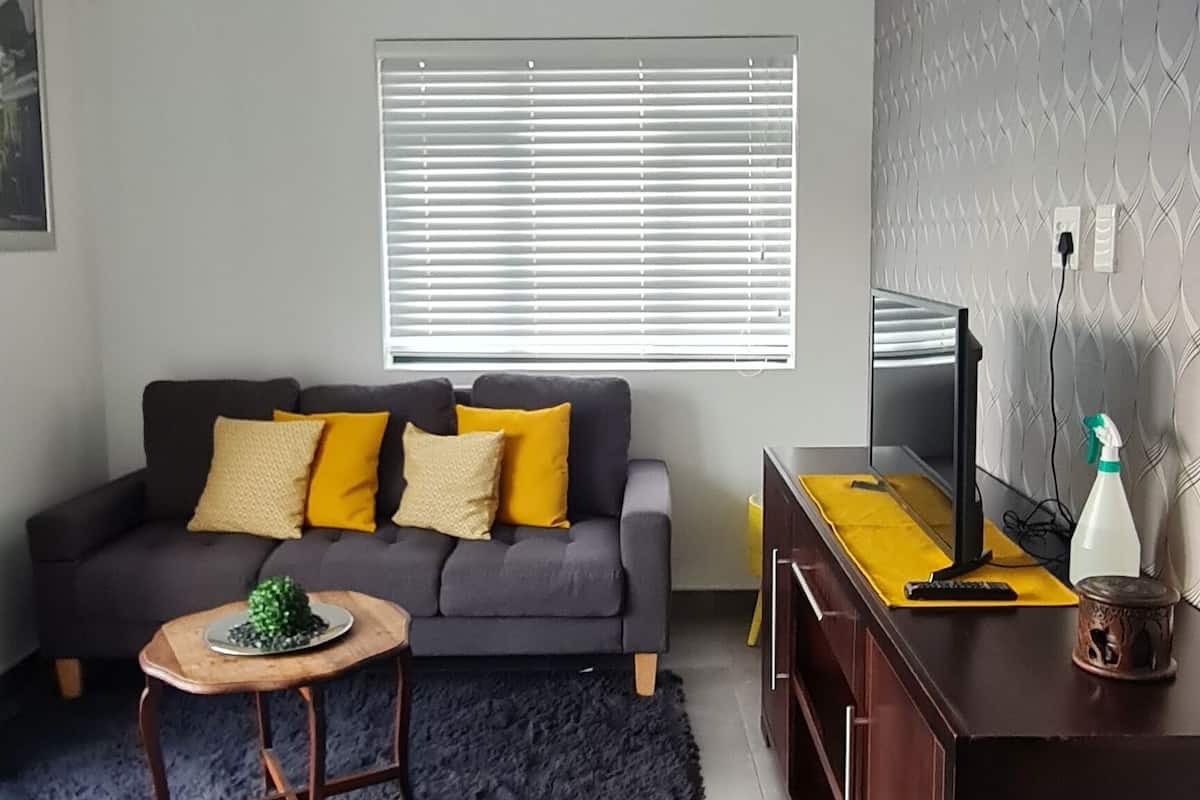 A living room with a grey sofa, a small round table, a dark rug, and a wooden cabinet with a TV and remote.