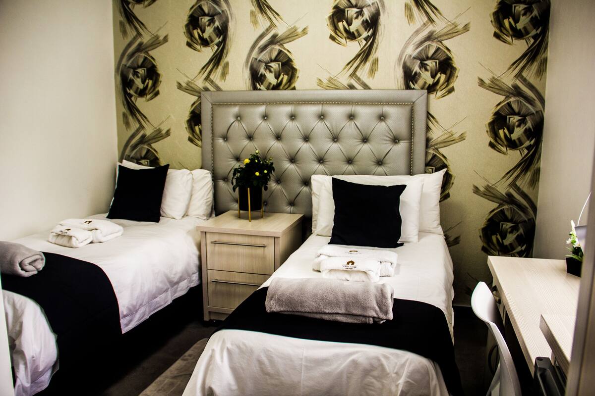 A hotel room with two beds, a small desk, and a nightstand with a vase of flowers.