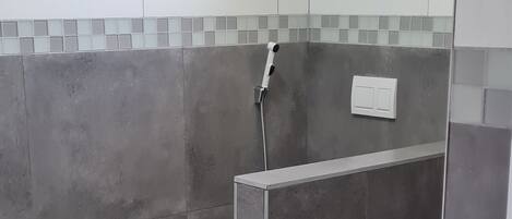 A modern bathroom with grey tiles, a shower, and a black rug.
