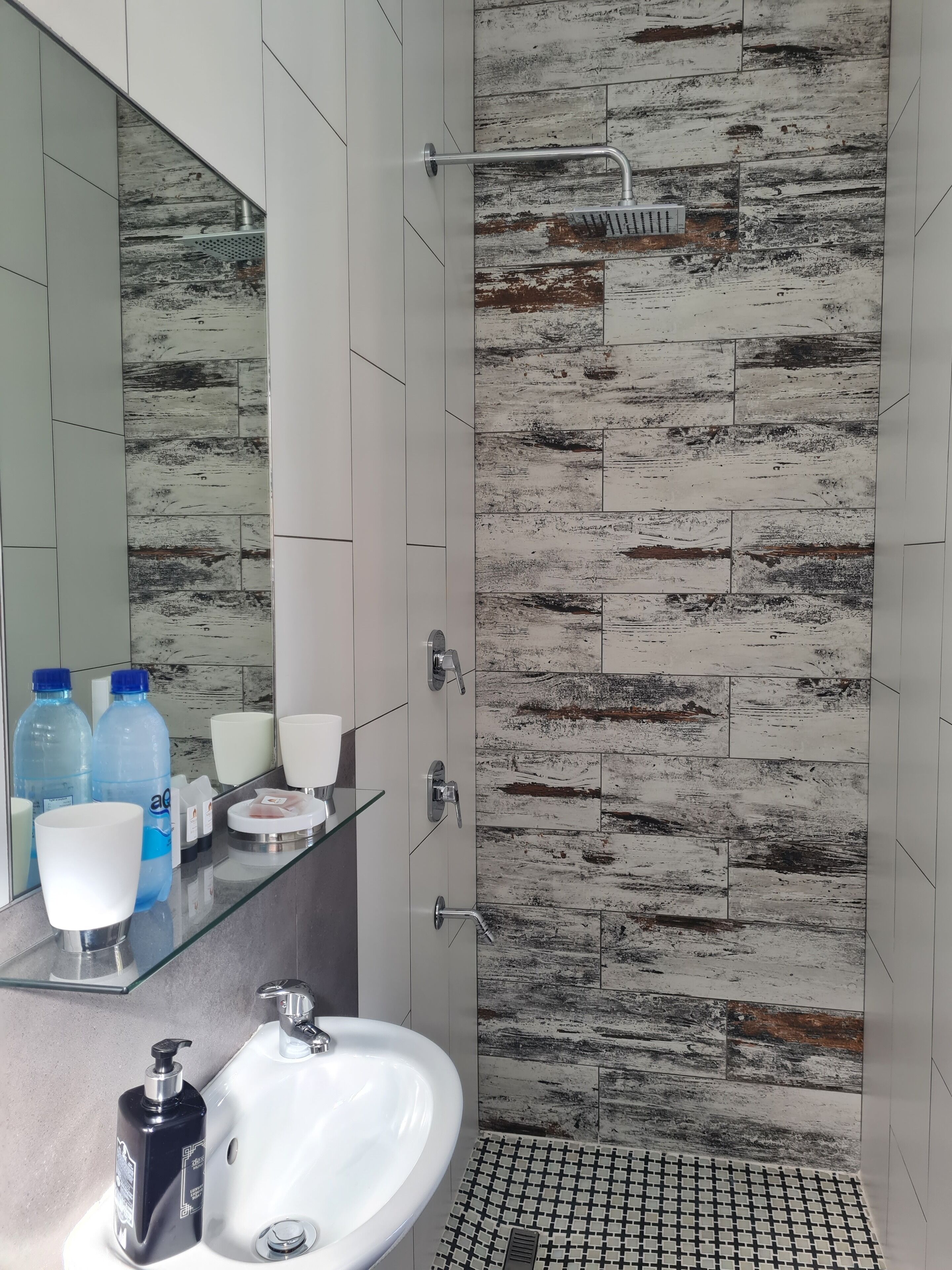 Une salle de bain moderne avec un lavabo en verre, un miroir et un espace douche agrémenté d’un mur au décor rustique.