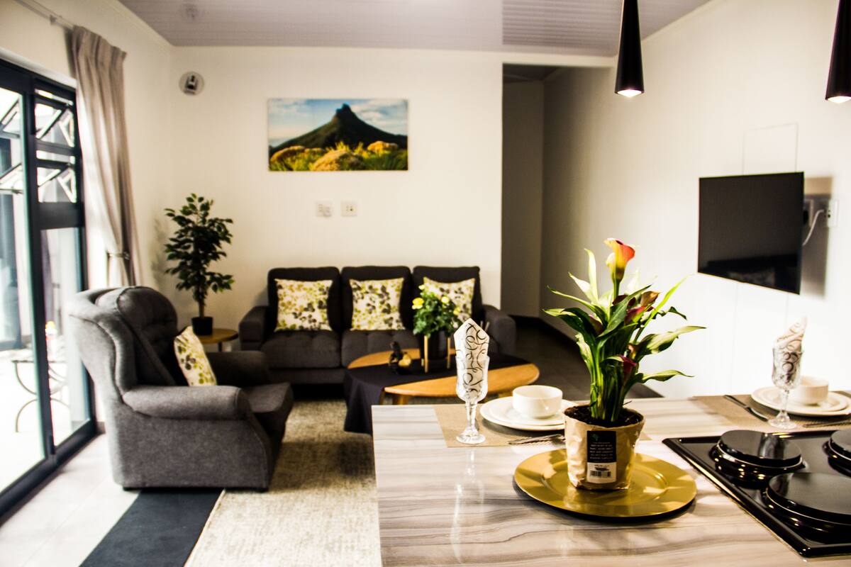 A modern living room with a sofa, armchairs, a coffee table, and a dining area with a TV.