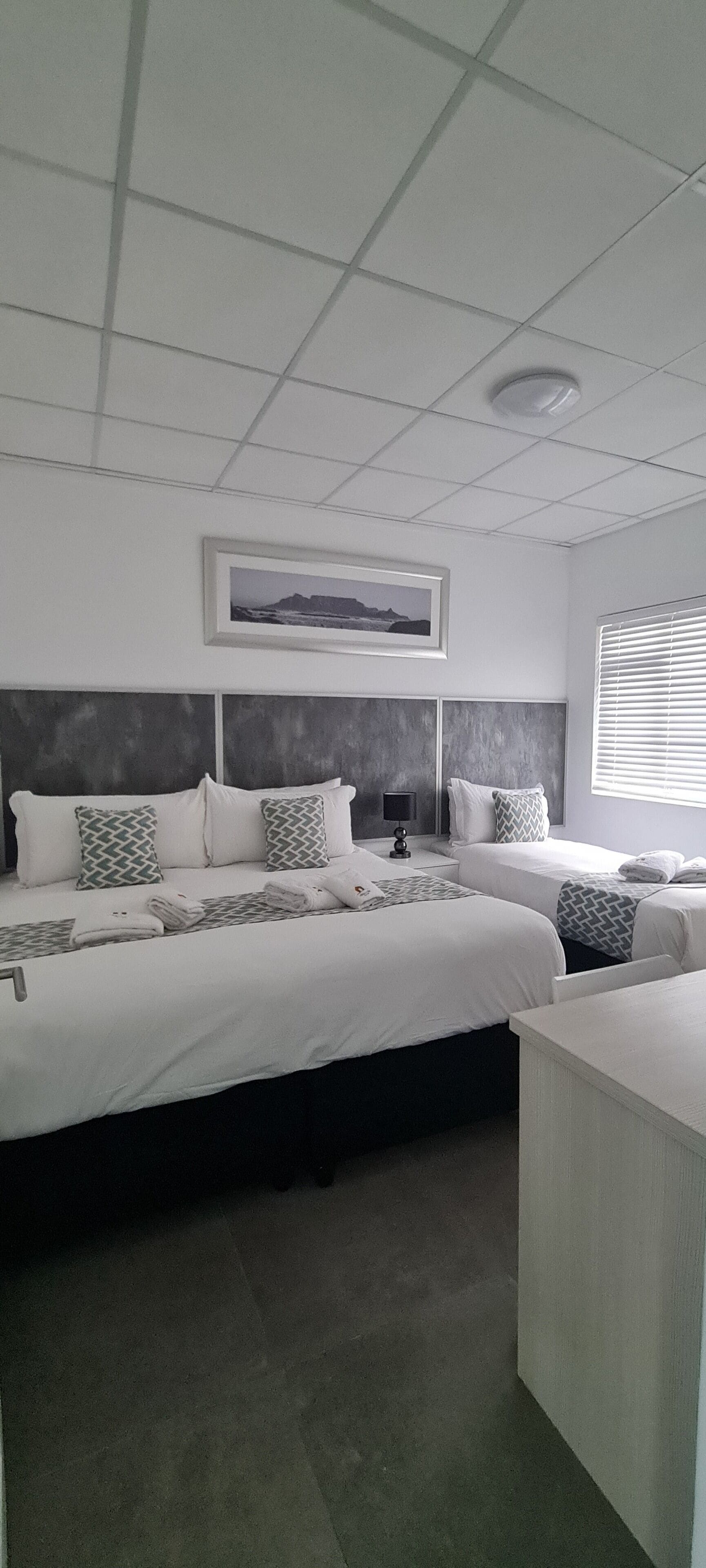 A hotel room with two beds, a framed picture on the wall, and a window with blinds.