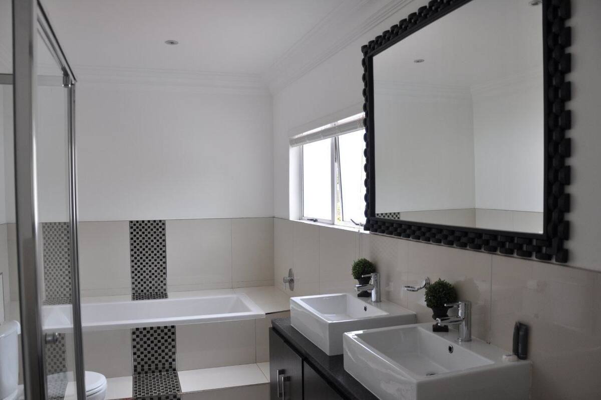 A modern bathroom with a large mirror, two sinks, a bathtub, and a shower.