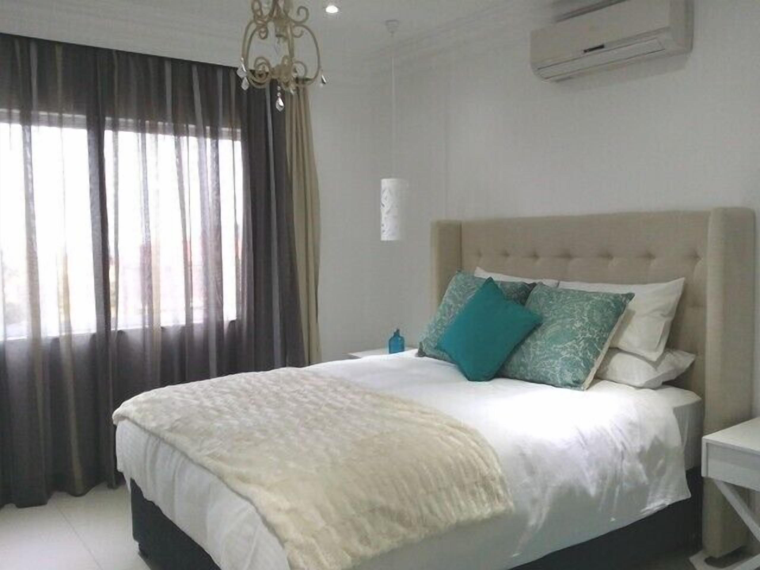 A bedroom with a large bed, a chandelier, and a window with curtains.