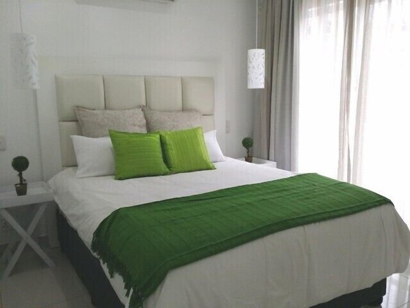 A neatly made bed with a green throw blanket and two green pillows, a white headboard, and a small bedside plant. - 34 on Milkwood (Umhlanga)