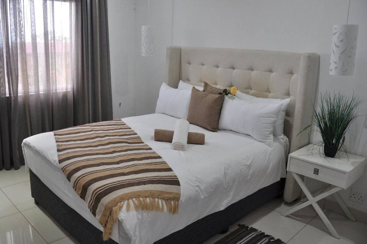 A neatly made bed with a striped blanket, a tufted headboard, and a bedside plant.