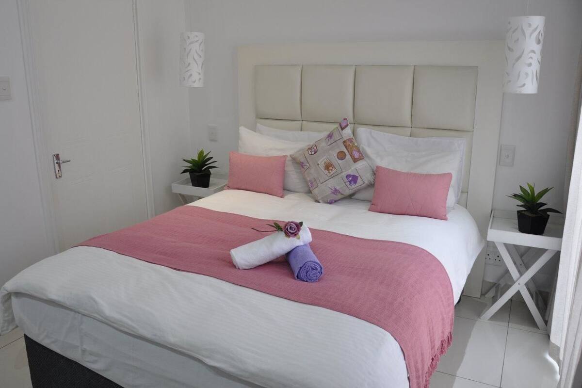 A neatly made bed with pink and white bedding, a headboard, and two bedside tables with potted plants.