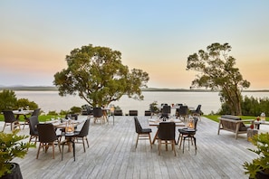 An outdoor dining area with tables and chairs, overlooking a body of water. - The Thatch House Hermanus (Hermanus)