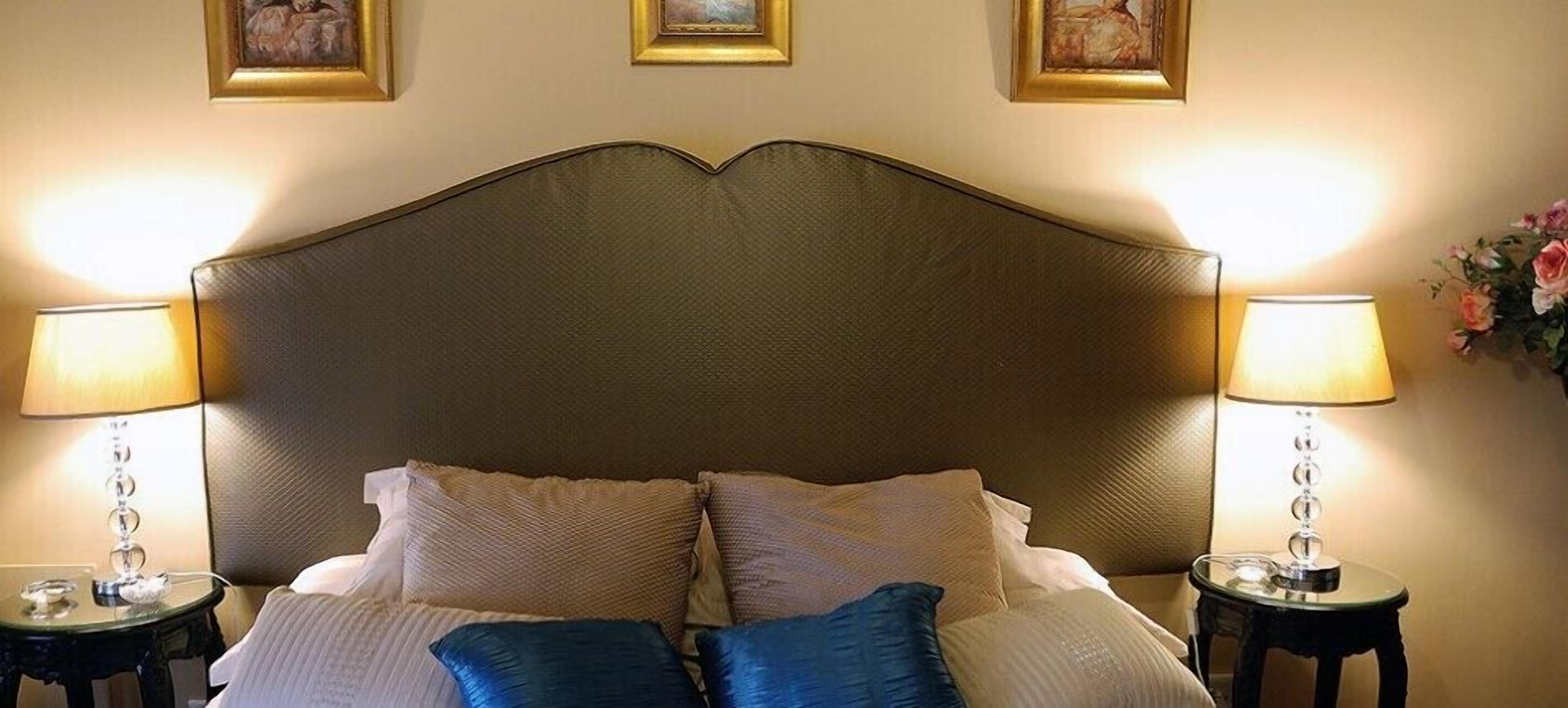 A neatly made bed with a headboard, two bedside lamps, and a small table with a vase of flowers.