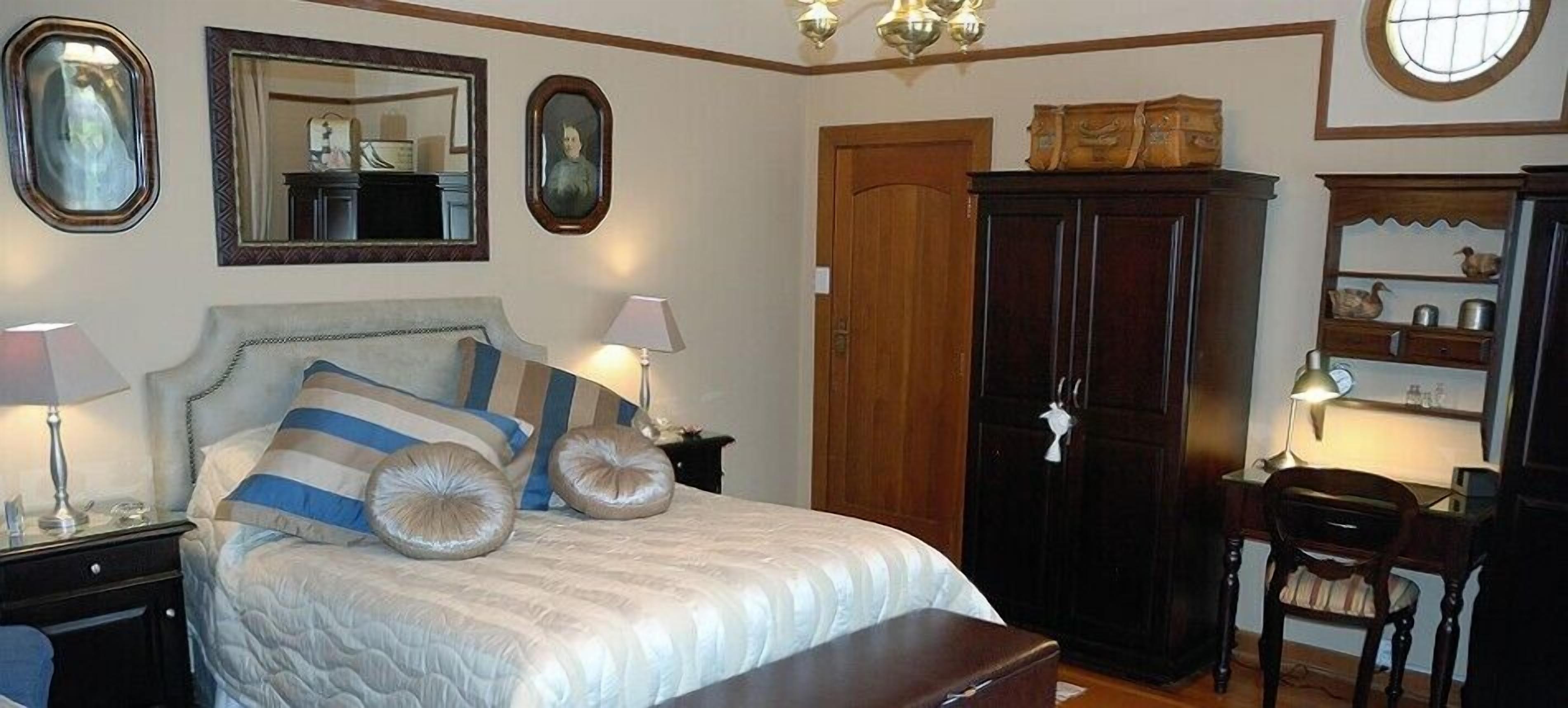 A bedroom with a bed, bedside lamps, a wardrobe, and a desk with a chair.