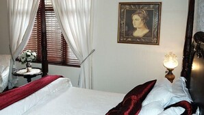 Et hotelværelse med en seng, en stol, et lille bord med en blomstervase, et portræt i ramme på væggen og en lampe.