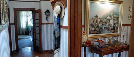 A hallway with a wooden door, a hat on a wall, and a painting on the wall.