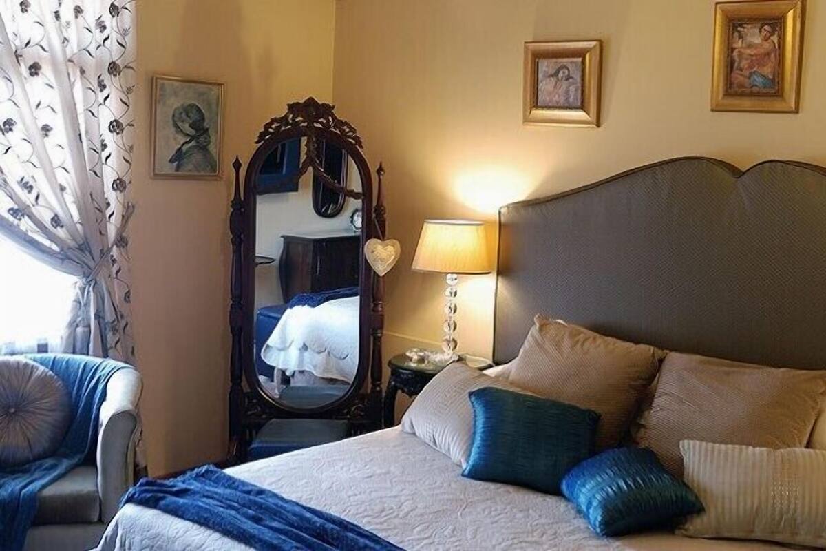 Una habitación de hotel con una cama grande, dos lámparas de noche, un espejo y obras de arte enmarcadas en las paredes.