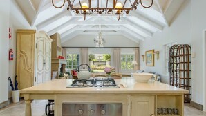 A spacious kitchen with a central island, a gas stove, an oven, and a chandelier. - Rose Cottage (Franschhoek)