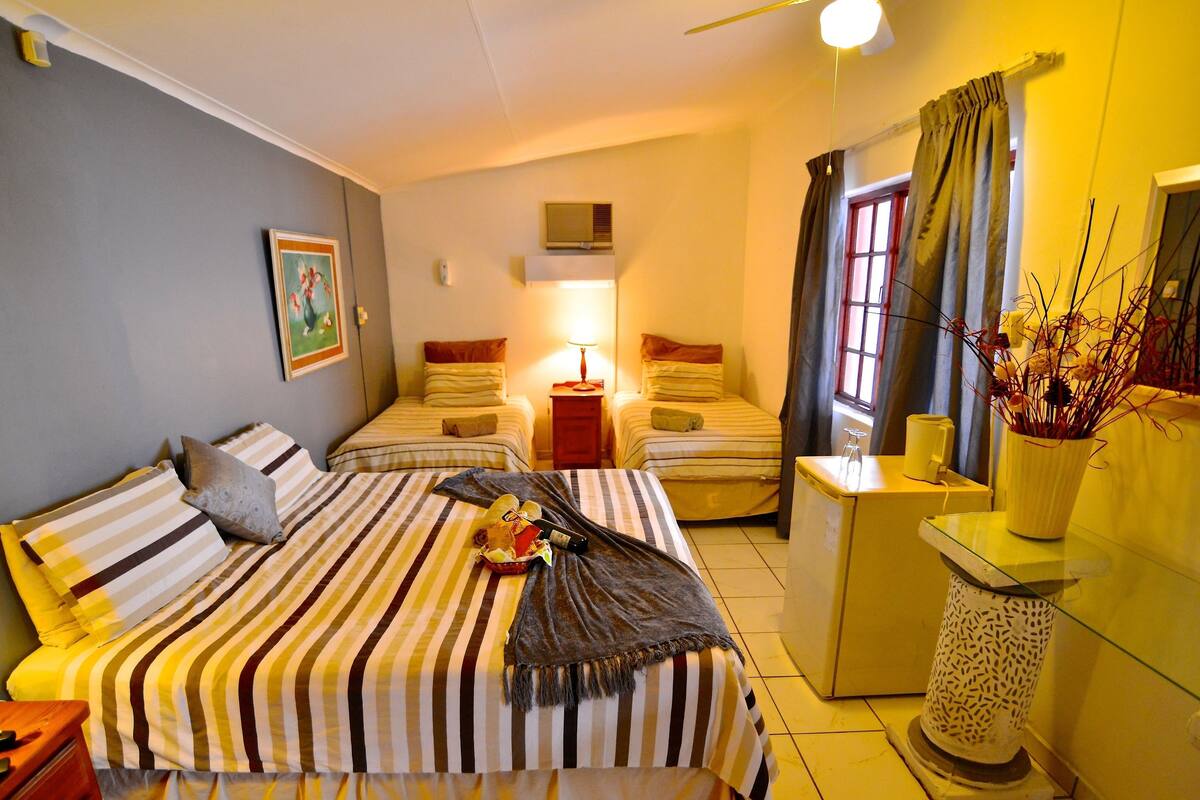 A hotel room with two beds, a desk, a lamp, a vase with flowers, and a painting on the wall.