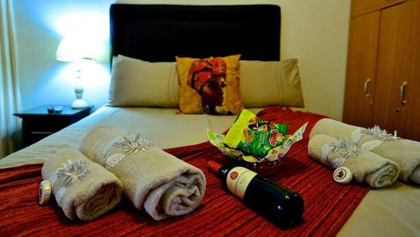 Cama bem arrumada com toalhas dobradas, uma garrafa de vinho e uma cesta de petiscos.
