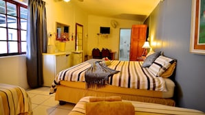 Quarto de hotel com cama, escrivaninha, cadeira, ventilador de teto e janela com cortinas.