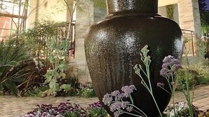 Una urna grande y oscura en un jardín, con un edificio de dos pisos al fondo.