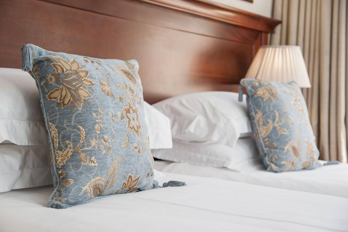 A neatly made bed with white linens and two decorative pillows with a blue and gold pattern.