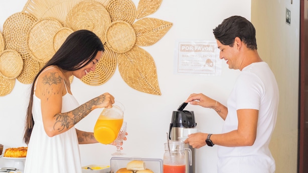 Une pièce décorée d’un grand élément mural tissé, avec une table sur laquelle sont disposés des aliments et une machine à café.
