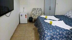 Une petite pièce simple, comprenant un lit, un téléviseur, un réfrigérateur et une armoire.