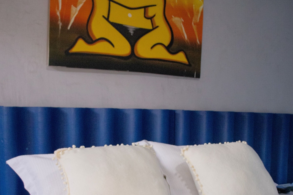 Habitación de hotel con cama, ropa de cama blanca y cabecera azul.