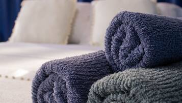 Una cama bien hecha con ropa blanca y dos toallas enrolladas en tonos azul y verde.